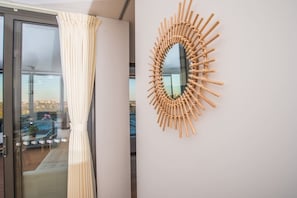 A room with a sliding glass door, a white curtain, and a wall-mounted mirror with a bamboo frame.