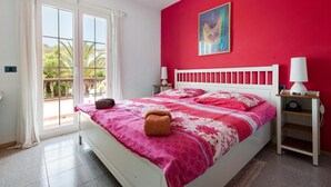 A bedroom with a bed, a nightstand, a window with curtains, and a red wall with a painting.