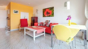 Uma sala de estar com um sofá vermelho, uma mesa amarela e uma poltrona branca.