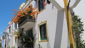 A row of white buildings with green window frames and yellow trim, featuring balconies with orange flowers. - Harbour 11 Apartment (Mogan)