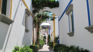 A narrow alleyway with white walls, blue and yellow trim, and green plants. - Harbour 11 Apartment (Mogan)