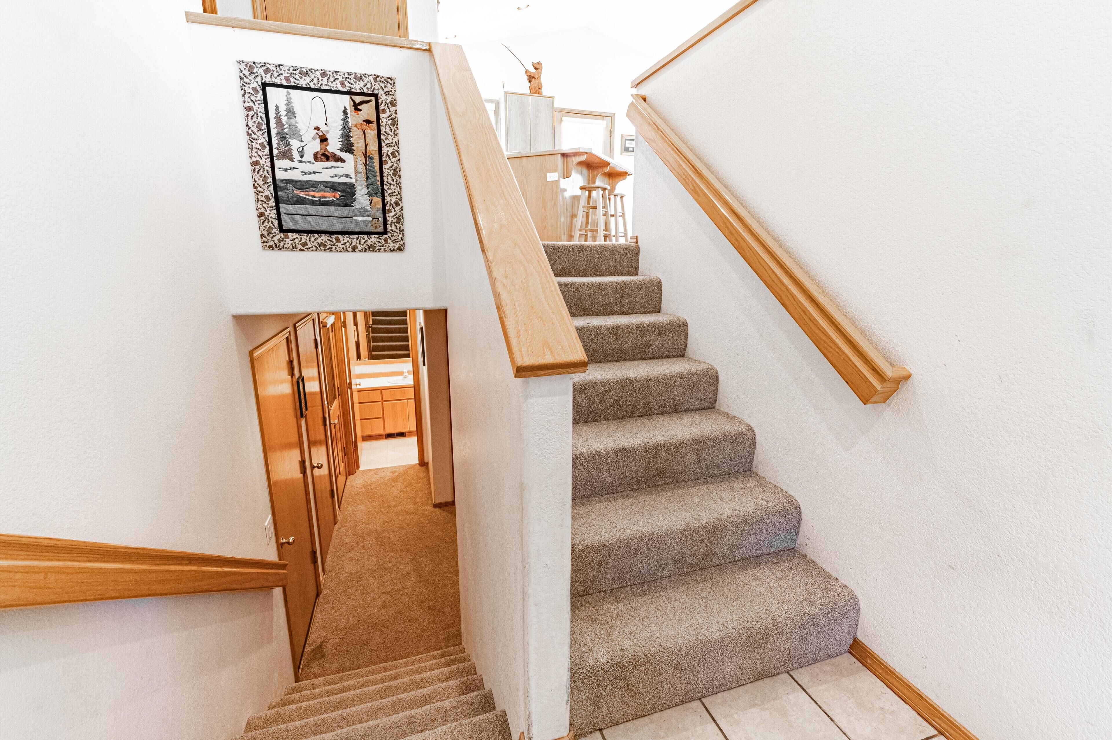 A staircase with wooden handrails and carpeted steps leading to a room with wooden cabinets and a framed picture on the wall.