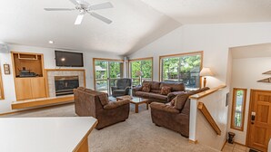 Amplia sala de estar con chimenea, asientos cómodos, televisor de pantalla plana y ventanas grandes que ofrecen vistas al exterior.