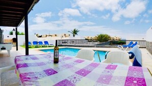 Un espace aménagé au bord de la piscine, avec une table dressée pour deux personnes, une bouteille de vin et des chaises longues.