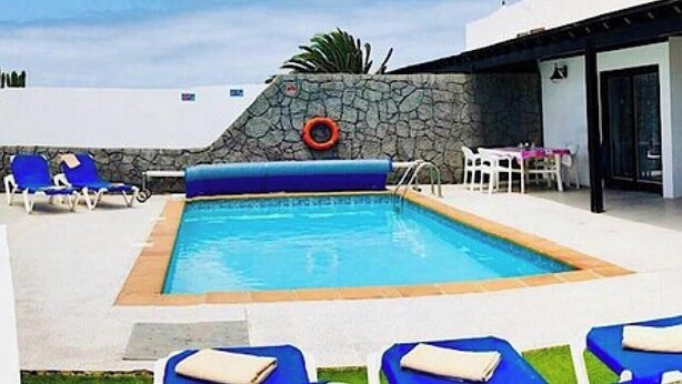 Une piscine avec des chaises longues, une table et un mur en pierre.