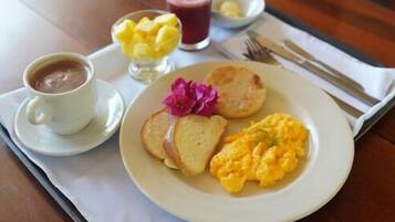 Uma bandeja de café da manhã com ovos mexidos, torradas, uma xícara de café e uma cesta de frutas sobre uma mesa de madeira.