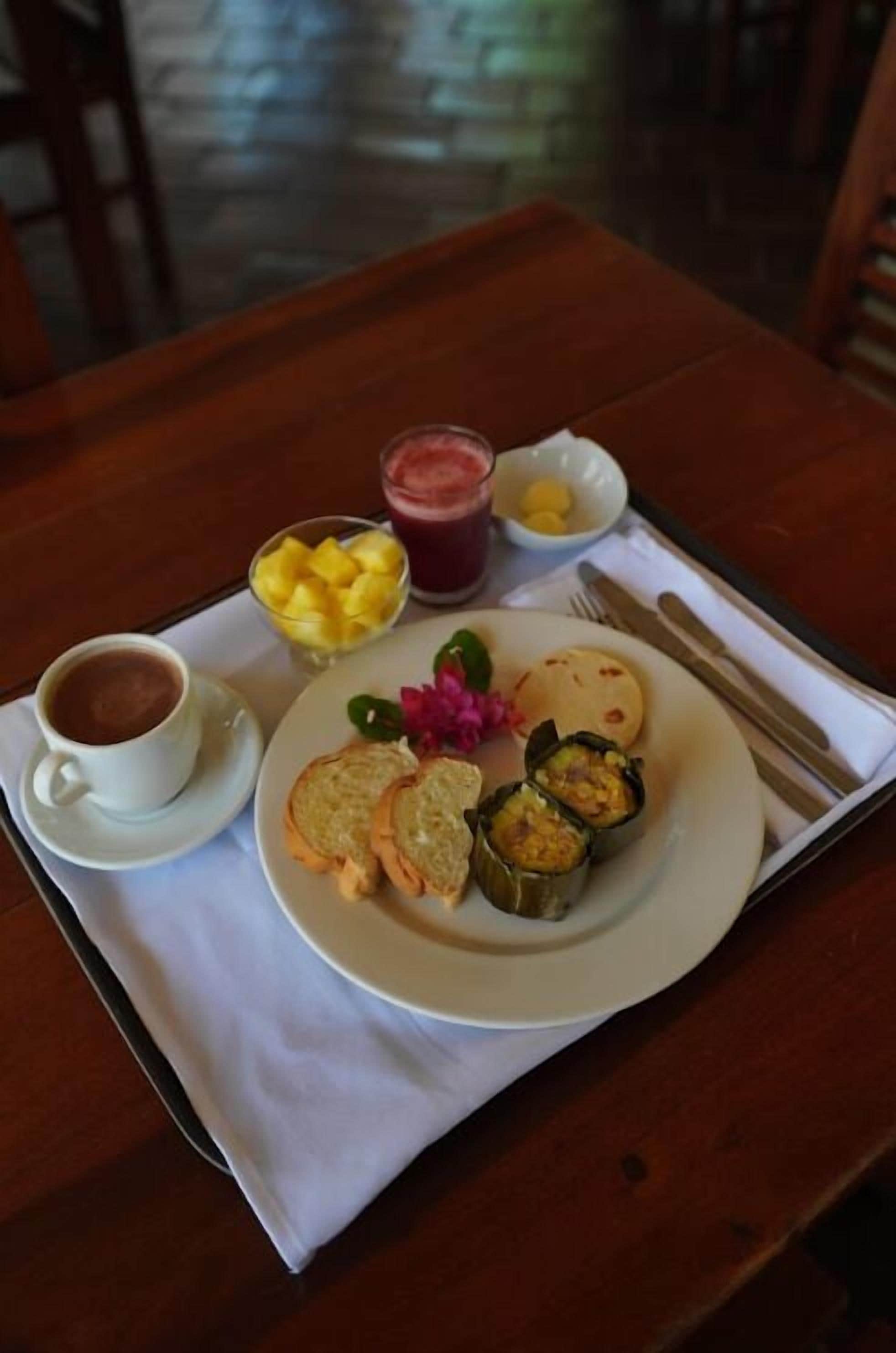Uma mesa com um prato de comida, uma xícara de café, uma tigela de fruta e um copo de suco.