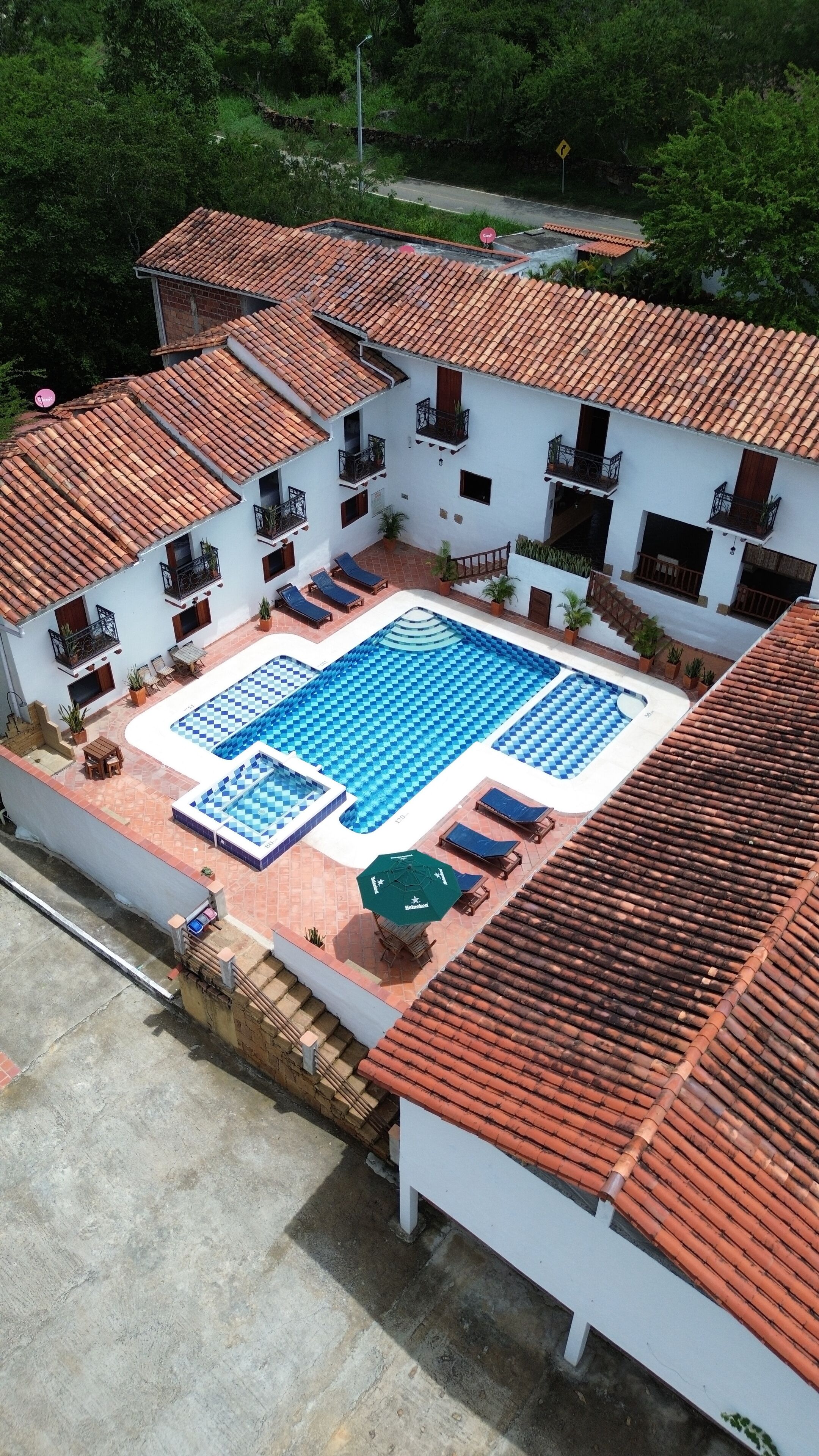A two-story building with a swimming pool, outdoor seating, and a red-tiled roof.