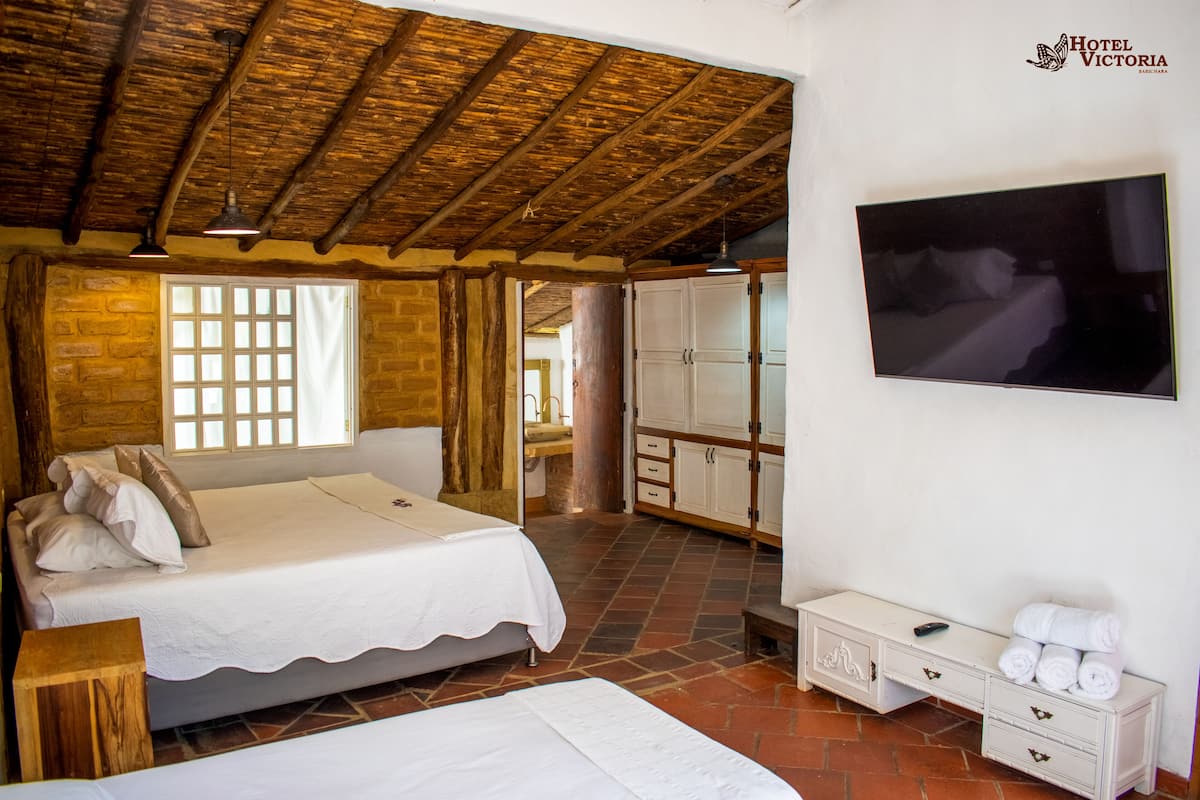 Ein Hotelzimmer mit rustikalem Holzboden, einem großen Bett mit weißer Bettdecke, einem an der Wand montierten Fernseher und einem kleinen Nachttisch mit Fernbedienung.