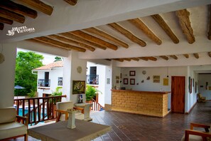A spacious hotel lobby with a wooden ceiling, a reception desk, and a view of the outdoor swimming pool.
