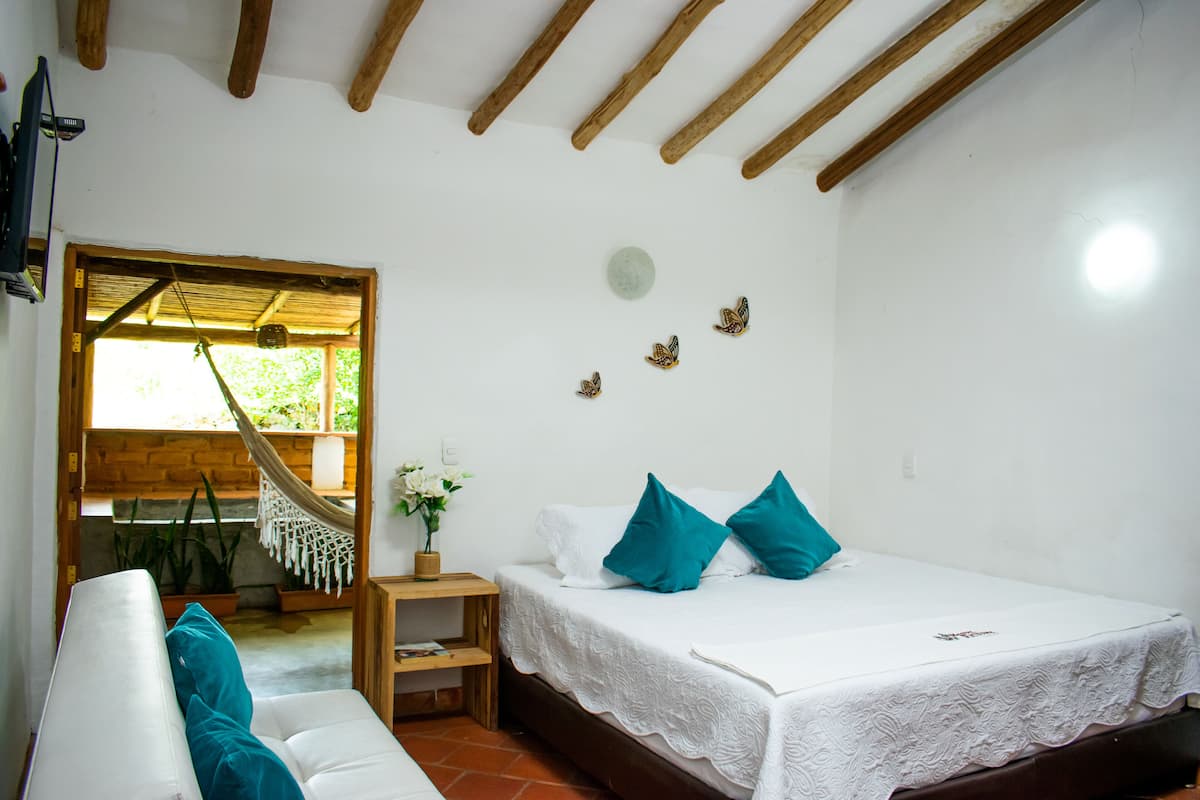 Ein Schlafzimmer mit Bett, einer Couch, einer Hängematte, einem kleinen Tisch und einer Zimmerpflanze.