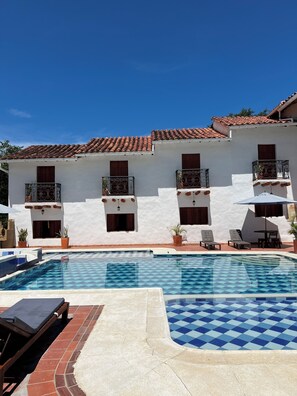 A hotel with a swimming pool, tiled roof, and white walls.