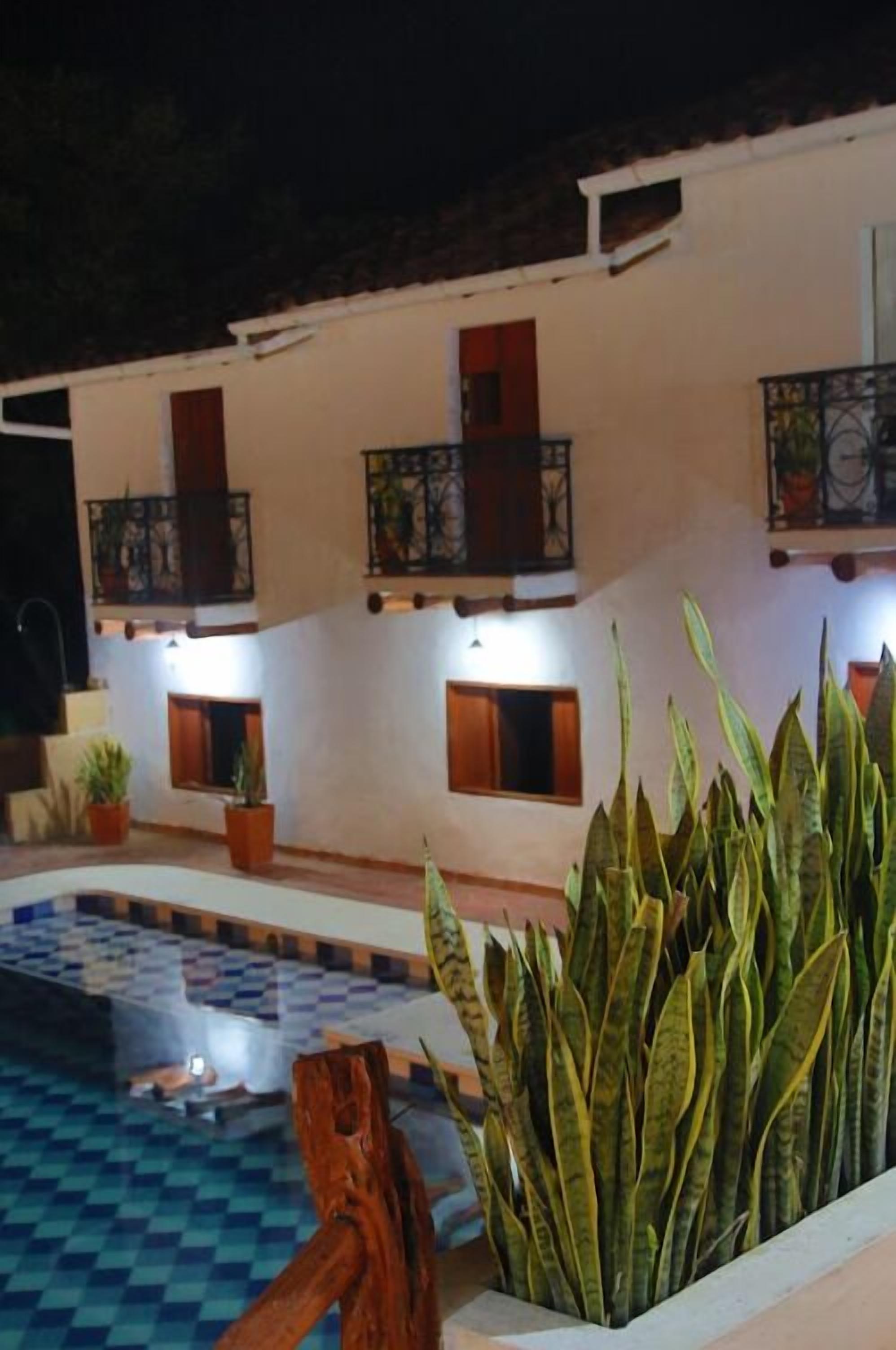 Zona de piscina con suelo a cuadros, plantas en macetas y un edificio blanco con balcones.