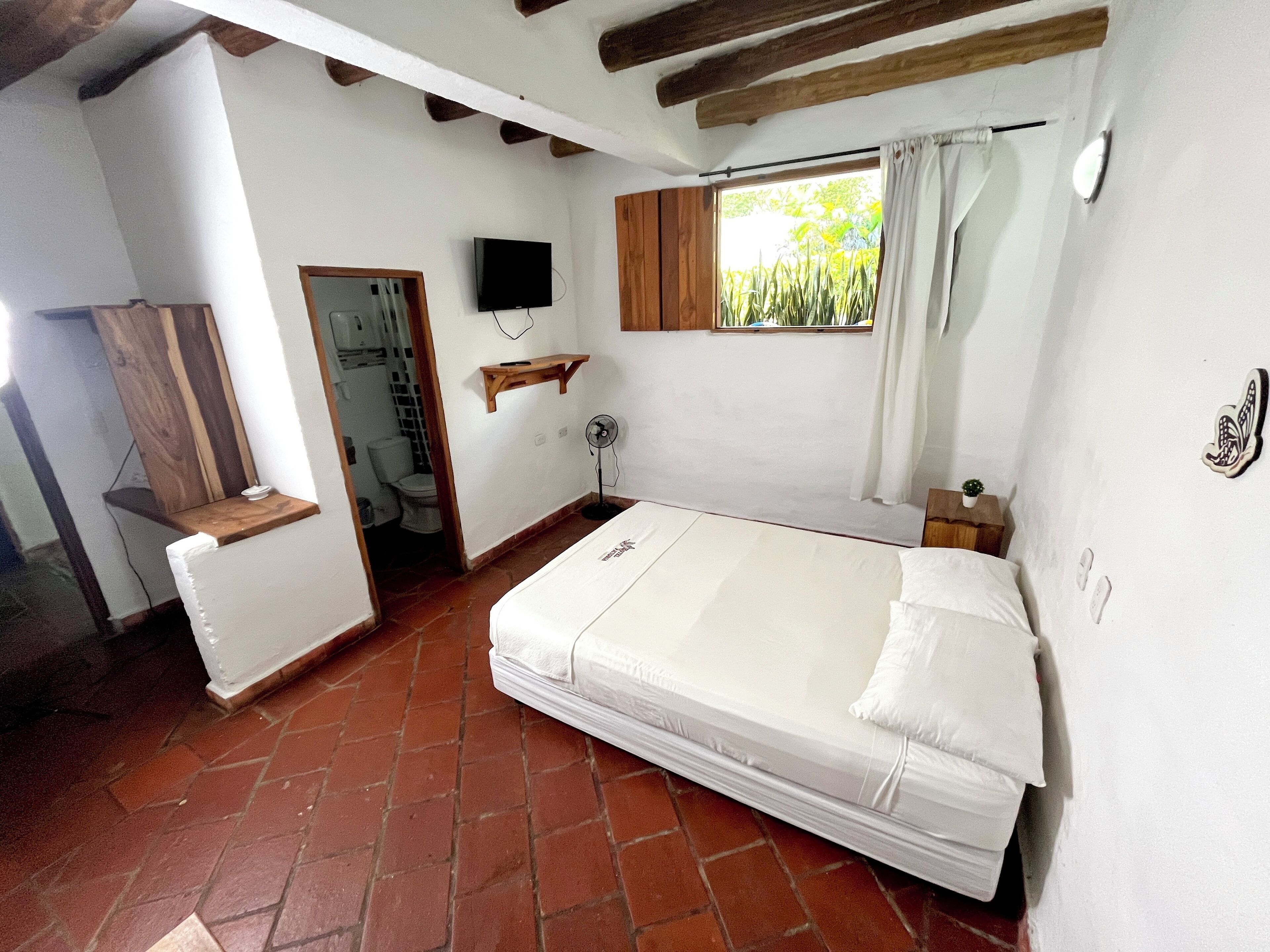 Une chambre avec un lit simple, une étagère en bois, une télévision et une fenêtre avec des rideaux.