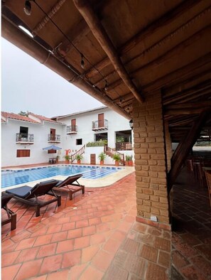 A pool area with lounge chairs, a brick wall, and a white building with balconies.