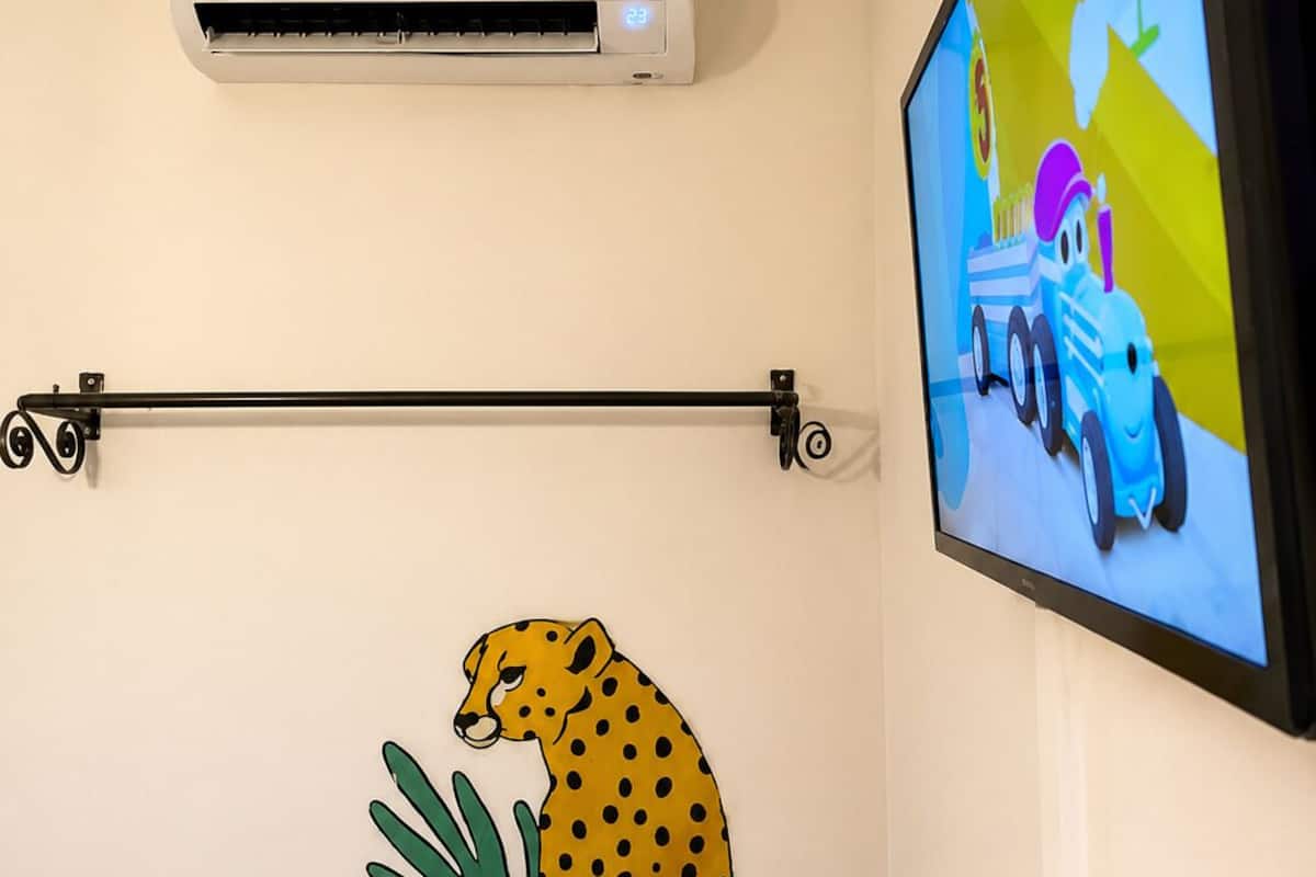 A room with a mounted TV displaying a children's show, a wall-mounted air conditioner, and a cheetah decoration.