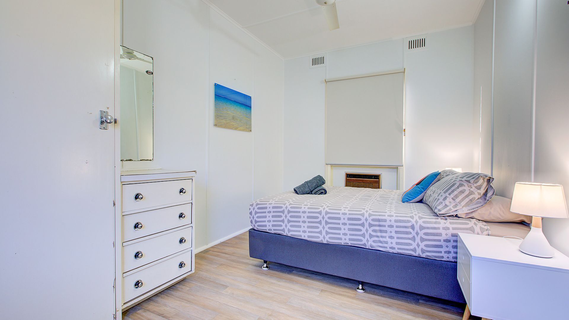 A bedroom with a bed, a dresser, a mirror, and a bedside table with a lamp.