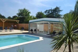 Une piscine dotée d’un espace couvert, de chaises longues et d’une terrasse en bois.