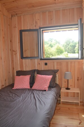 Une chambre dans une cabane en bois, avec un lit, des oreillers, une table de chevet et une fenêtre.