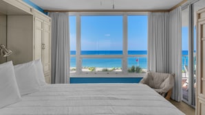 Een slaapkamer met een groot bed, een plafondventilator en uitzicht op zee door een raam.