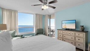 A hotel room with a large bed, a ceiling fan, a television, and a view of the ocean. - On the Beach, Pool, Huge TV, 3 Balconies, Umbrellas and Chairs Included (Miramar Beach)