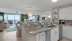 Une cuisine moderne dotée d’un grand îlot central, un coin repas offrant une vue dégagée et un salon avec une grande fenêtre donnant sur l’océan.
