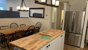 A kitchen with a wooden island, white cabinets, a stainless steel refrigerator, and a dining area with wooden chairs. - Newly renovated in-town Bar Harbor, five bdrm apartment. Walk to shore & shops. (Bar Harbor)
