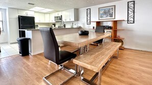 Une cuisine moderne avec des armoires blanches, un réfrigérateur noir et un four à micro-ondes. On y trouve une table à manger avec un banc, une chaise noire et un ventilateur de plafond.