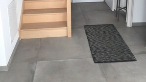 A wooden staircase leading to a door, a black doormat, and a small stool near a window. - New house with swimming pool and large outdoor terrace. (VENCE)