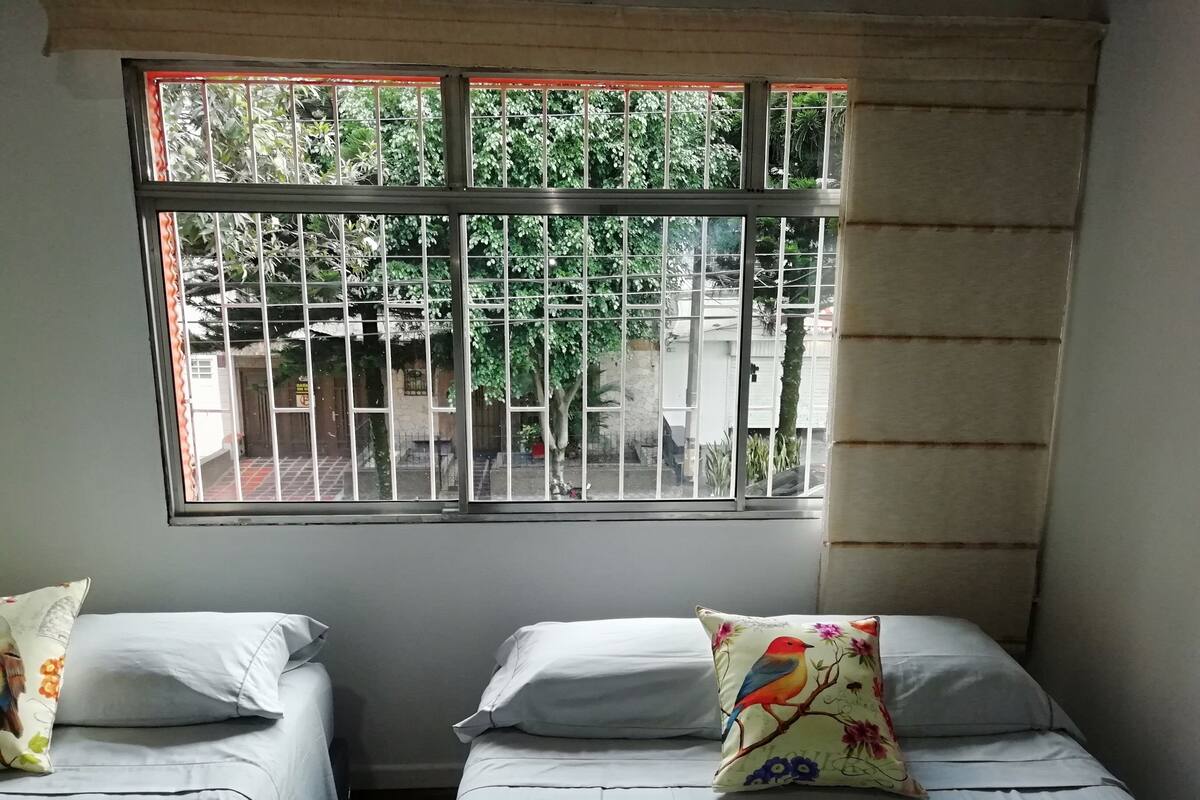 Une chambre avec deux lits, une fenêtre avec des barreaux et une vue sur la verdure.