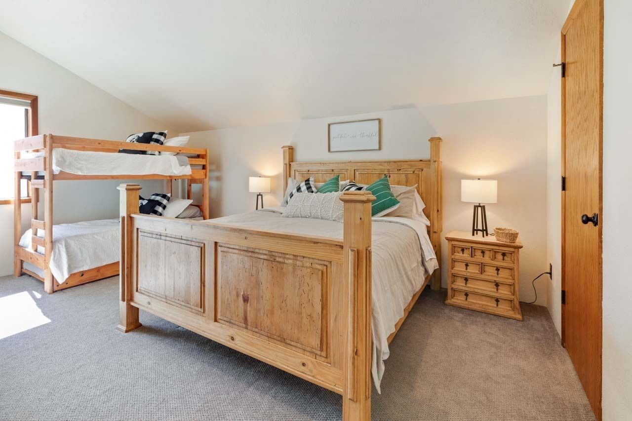 Ein Schlafzimmer mit einem hölzernen Bett, einem Etagenbett, einem Nachttisch mit Lampe und einer Kommode.