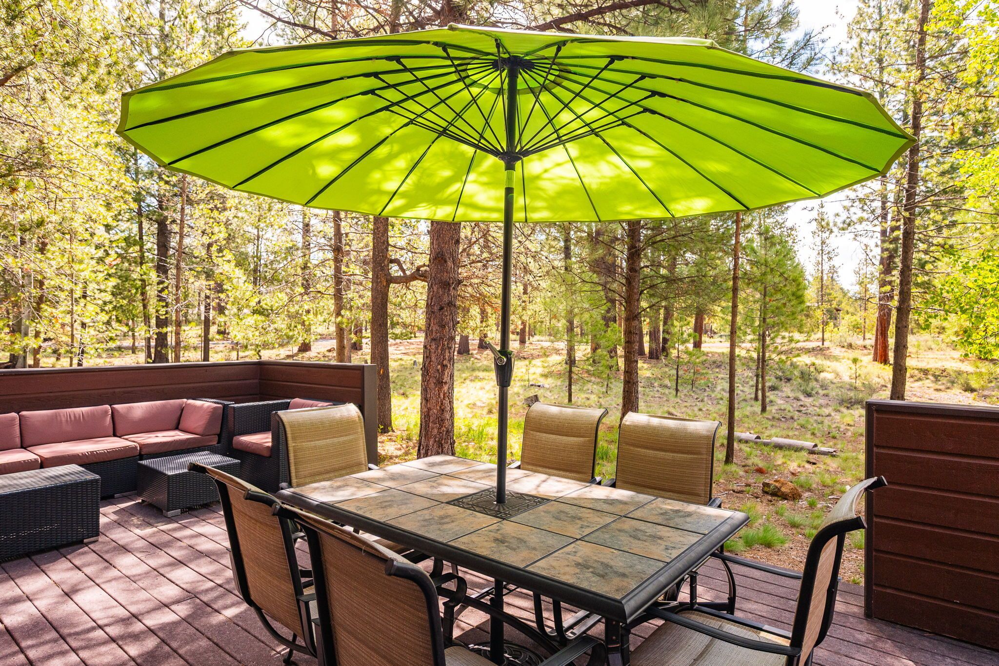An outdoor patio with a table and chairs, surrounded by a wooden deck and a green umbrella.