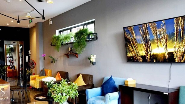 Eine moderne Hotelhalle mit Empfangstresen, einer Sitzecke mit Sofas, einem großen Flachbildfernseher und dekorativen Pflanzen.