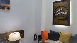 Ein modernes Zimmer mit einem hölzernen Kopfende, einer Nachttischlampe, einem gerahmten Kunstwerk mit dem Wort 'home' und einem Sofa mit bunten Kissen.