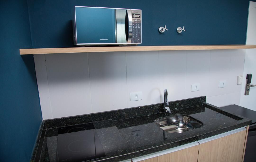 A kitchen with a black countertop, a built-in microwave, and a stainless steel sink.
