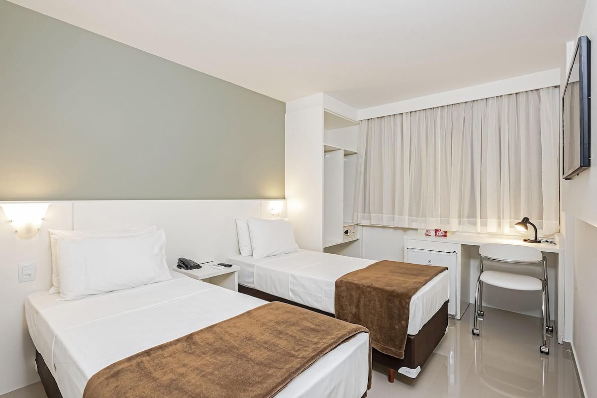 Une chambre d’hôtel avec deux lits, un bureau, une chaise, un miroir et une salle de bain.