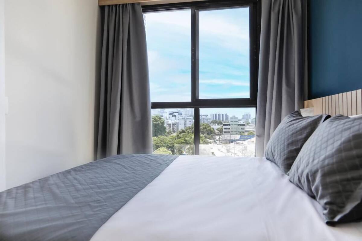 Une chambre d’hôtel avec un lit, des rideaux et une vue sur le paysage urbain, visible à travers une grande fenêtre.