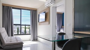 Een moderne woonkamer met een glazen tafel, een bank en een aan de muur bevestigde televisie.