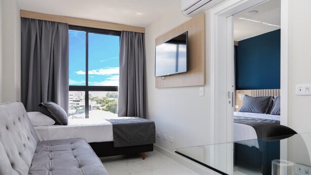 Een moderne hotelkamer met een groot raam, een flatscreen televisie aan de wand, een bank en een bed met hoofdeinde.