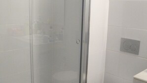 Ett badrum med en dusch som är avskärmad med glasväggar, en toalett och en väggmonterad spolknapp.