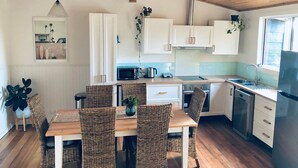 A modern kitchen with white cabinets, a wooden dining table, wicker chairs, and a stainless steel refrigerator. - Bush Hideaway (Binalong Bay)
