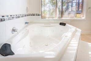 A white bathtub with a black seat, a showerhead, and a window with blinds.