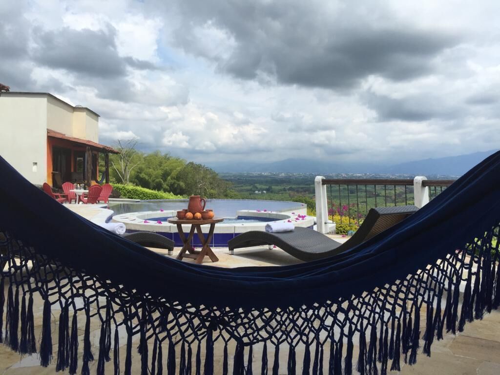 A hammock on a balcony overlooking a hot tub and outdoor seating area with a scenic view.