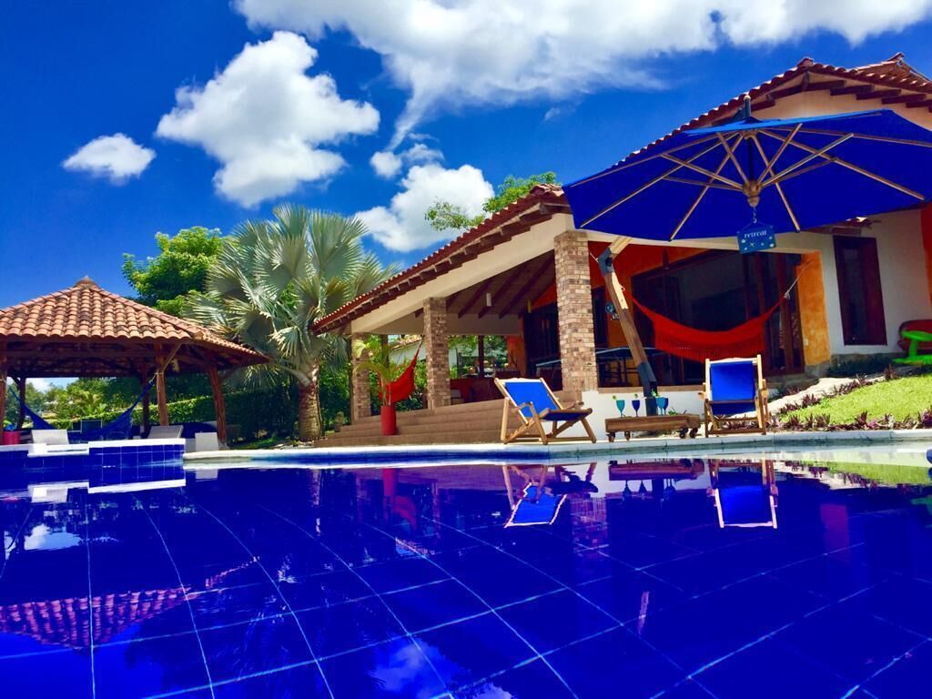 Una piscina con sillas de descanso y sombrillas, rodeada por un edificio de tejado de baldosas y un porche cubierto.
