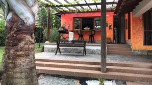 A covered outdoor seating area with a bench, steps leading to a building with a red exterior, and a palm tree. - Casa Mar Verde (Montenegro)