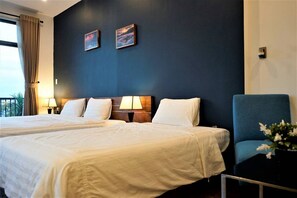 A hotel room with two beds, a dark blue accent wall, and two framed pictures.