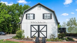 Un edificio de estilo granero blanco con una puerta de garaje grande, dos ventanas y un letrero que dice 'Red Bud Cove Barnhouse Suites'.