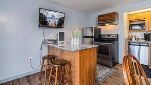 Una cocina moderna con una isla central, taburetes de madera, horno empotrado y un televisor montado en la pared.