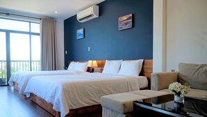 A hotel room with two beds, a sofa, a small table with a vase, and a balcony with curtains. - OASIS-NEAR BEACH-STUDIO ROOM (Da Nang)