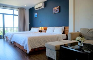 A hotel room with two beds, a sofa, a small table with a vase, and a balcony with curtains.